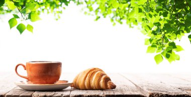 Kahve fincanı ve kruvasan ahşap masada. Açık hava bahçesi.