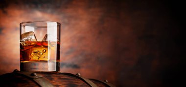 Glass of whiskey with ice cubes on the old barrel. With copy space on wooden background clipart