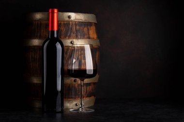 Şarap fıçısının önünde kırmızı şarap şişesi ve cam var.