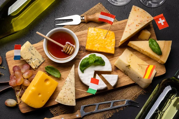 Various cheese with different Europe flags on board and white wine. Flat lay