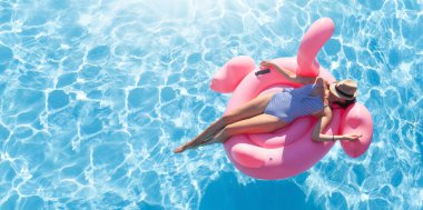Woman relaxing on pink flamingo inflatable ring. Sunny pool vacation. With copy space