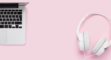 Headphones and laptop on pink background. Flat lay with copy space
