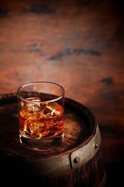 Glass of whiskey with ice cubes on the old barrel. With copy space on wooden background