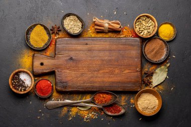 Empty cutting board over various spices on stone table. Frame with copy space for your menu or recipe