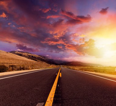 Kırsal alanda, gün batımında dramatik gökyüzü ile boş asfalt yol