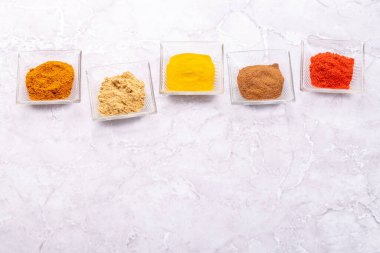 Various dried spices in small bowls on stone table with copy space