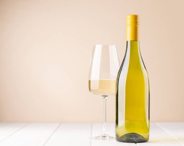 White wine bottle and glass in front of beige background. With copy space