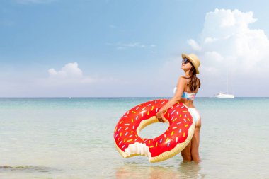 Beautiful young woman with inflatable donut ring relaxing on sea beach. Summer vacation. With copy space