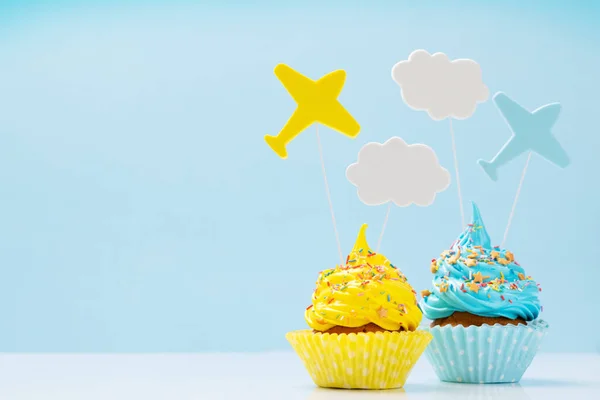 Yellow and blue cream cupcakes with decor on blue background with copy space