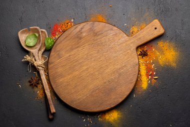 Empty cutting board over various spices on stone table. Frame with copy space for your menu or recipe