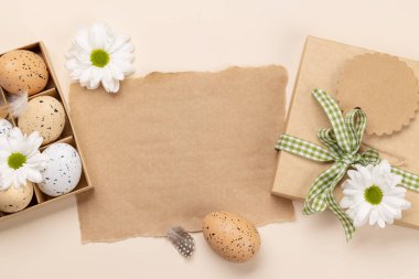 Gift box, Easter eggs and flowers on a beige background with space for your greetings. Flat lay