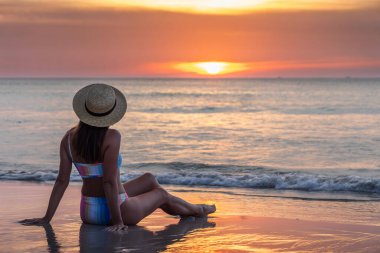 Woman sitting on the sea beach and enjoying sunset