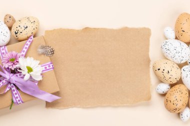 Gift box, Easter eggs and flowers on a beige background with space for your greetings. Flat lay