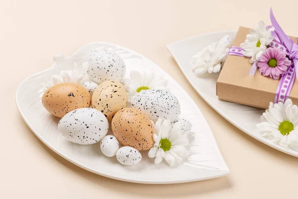 プレート上のイースターの卵と花とベージュの背景上のギフトボックス — ストック写真