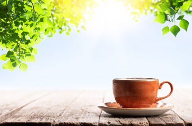 Kahve fincanı ahşap masada. Açık hava güneşli bahçe ve ağaç yaprakları