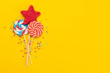 Various candy sweets and lollipops on yellow background and copy space for your text. Flat lay