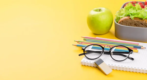 School supplies, stationery, and lunch box on yellow background. Education and nutrition. With blank space for your text