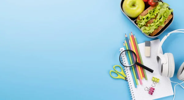 School supplies, stationery, and lunch box on blue background. Education and nutrition. Flat lay with blank space