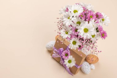 Gift box, Easter eggs and flowers bouquet on a beige background with space for your greetings