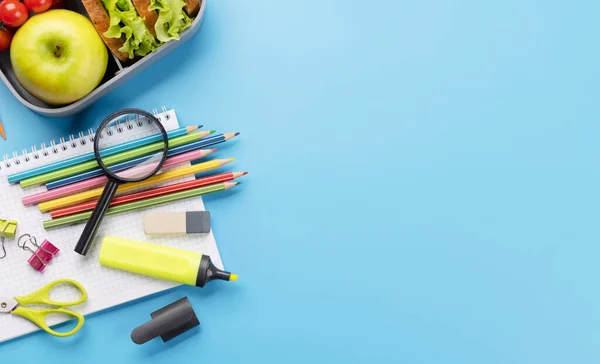 School supplies, stationery, and lunch box on blue background. Education and nutrition. Flat lay with blank space