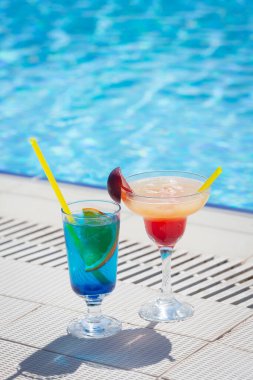 Yüzme havuzunun kenarında iki renkli kokteyl bardağı. Kopyalama alanı ile