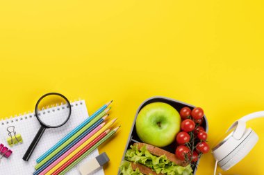 School supplies, stationery, and lunch box on yellow background. Education and nutrition. Flat lay with blank space