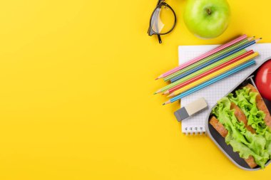 School supplies, stationery, and lunch box on yellow background. Education and nutrition. Flat lay with blank space