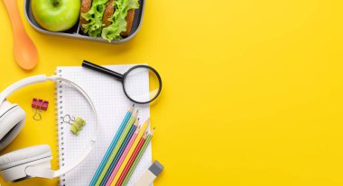 School supplies, stationery, and lunch box on yellow background. Education and nutrition. Flat lay with blank space