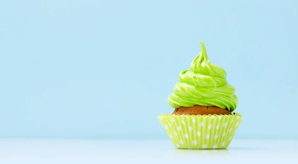 Green cream cupcake on blue background with copy space