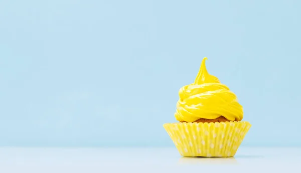 Yellow cream cupcake on blue background with copy space