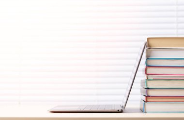 Dizüstü bilgisayar ve kitap yığını arka planda pencere perdeleri olan ve boşluğu kopyalayan