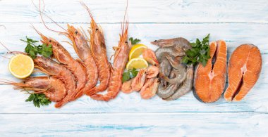 Karides, langoustine ve alabalık bifteği gibi taze deniz ürünleri. Düz, mavi ahşap masanın üzerinde.