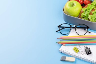 Okul malzemeleri, kırtasiye malzemeleri ve mavi arka planda beslenme çantası. Eğitim ve beslenme. Boş alanla