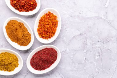 Various dried spices in small bowls on stone table with copy space. Flat lay