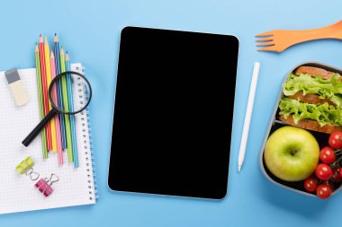 Boş ekranlı tablet, okul malzemeleri, kırtasiye malzemeleri ve mavi arka planda beslenme çantası. Eğitim ve beslenme. Metnin ya da uygulaman için boş alanı olan düz uzan