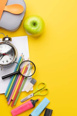 School supplies, stationery, and lunch box on yellow background. Education and nutrition. Flat lay with blank space