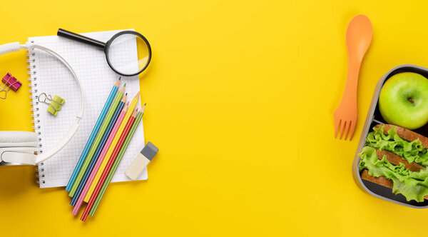 School supplies, stationery, and lunch box on yellow background. Education and nutrition. Flat lay with blank space
