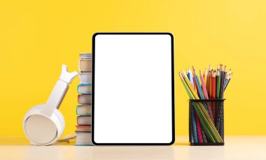 Renkli kalemler ve bir yığın kitapla dolu bir tablet. Metnin ya da uygulaman için boş ekranla