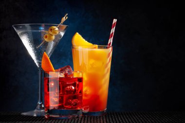 Negroni, tequila sunrise and martini cocktails on dark background with copy space clipart