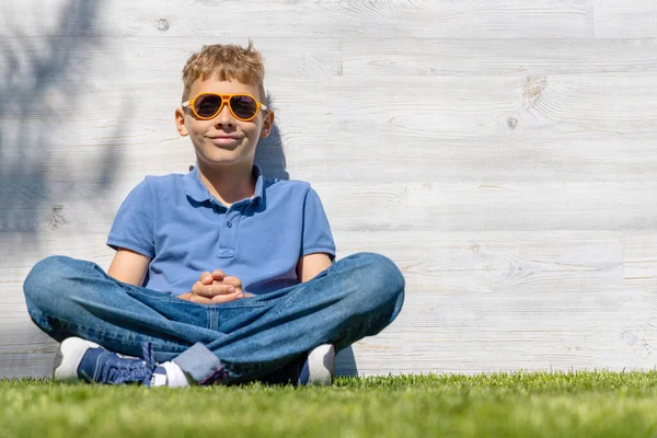 Ein Schuljunge Mit Sonnenbrille Sitzt Auf Einer Wiese Mit Kopierraum — Stockfoto