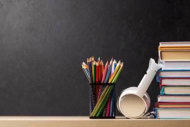 Renkli kitap yığınları, kalemler ve kulaklıklar. Masada metnin için yer var.