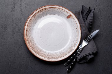 Empty plate with fork and knife on dark stone table. Flat lay with copy space