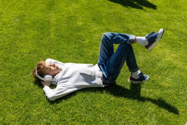 Çimenlerde dinlenen, kulaklıkla müzik dinleyen bir çocuk.