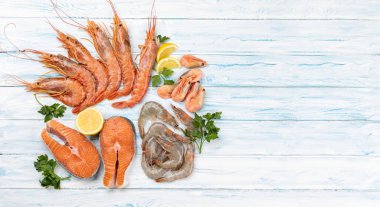 Karides, langoustine ve alabalık bifteği gibi taze deniz ürünleri. Fotokopi alanı olan mavi ahşap masa üzerinde düz uzandı