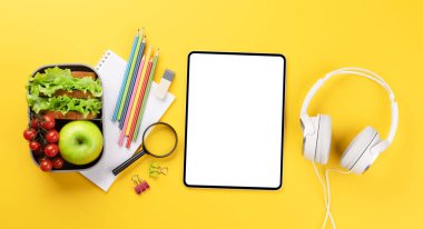 Boş ekranlı tablet, okul malzemeleri, kırtasiye malzemeleri ve sarı arka planda beslenme çantası. Eğitim ve beslenme. Metnin ya da uygulaman için boş alanı olan düz uzan