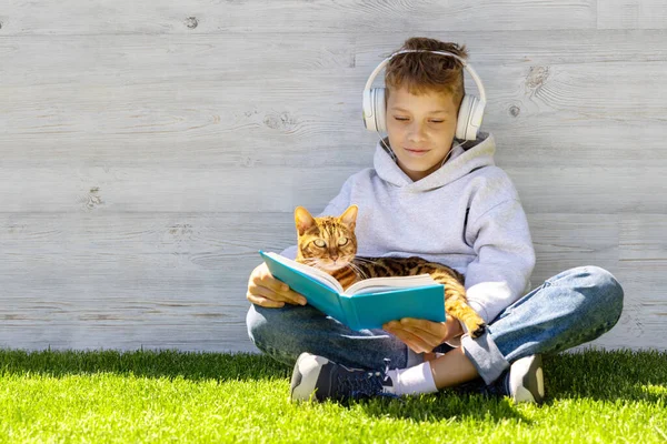 A boy with cat reading a book on a grassy field