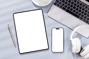 Ofis masasında boş ekranlı tablet ve akıllı telefon. Güneşli ışıklandırmalı düz çalışma alanı ve kopyalama alanı