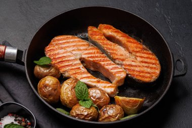 Kızarmış somon bifteği ve patates kızartma tavasında cızırdıyor.