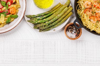 Taze domates ve aromatik fesleğen yapraklarıyla süslenmiş nefis bir tabak İtalyan makarnası ızgara kuşkonmaz ve karidesli makarna. Kopyalama alanı olan düz