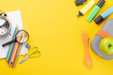 School supplies, stationery, and lunch box on yellow background. Education and nutrition. Flat lay with blank space